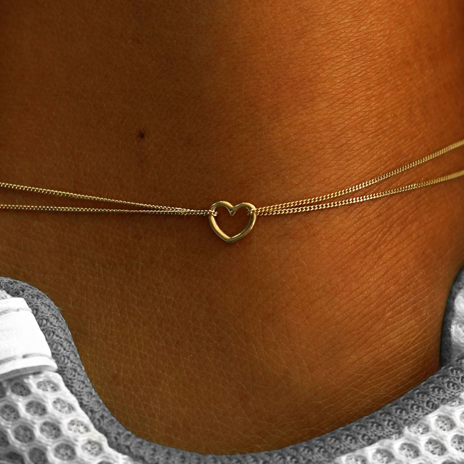 Close up view of a model's ankle wearing a 14k yellow gold Heart Anklet