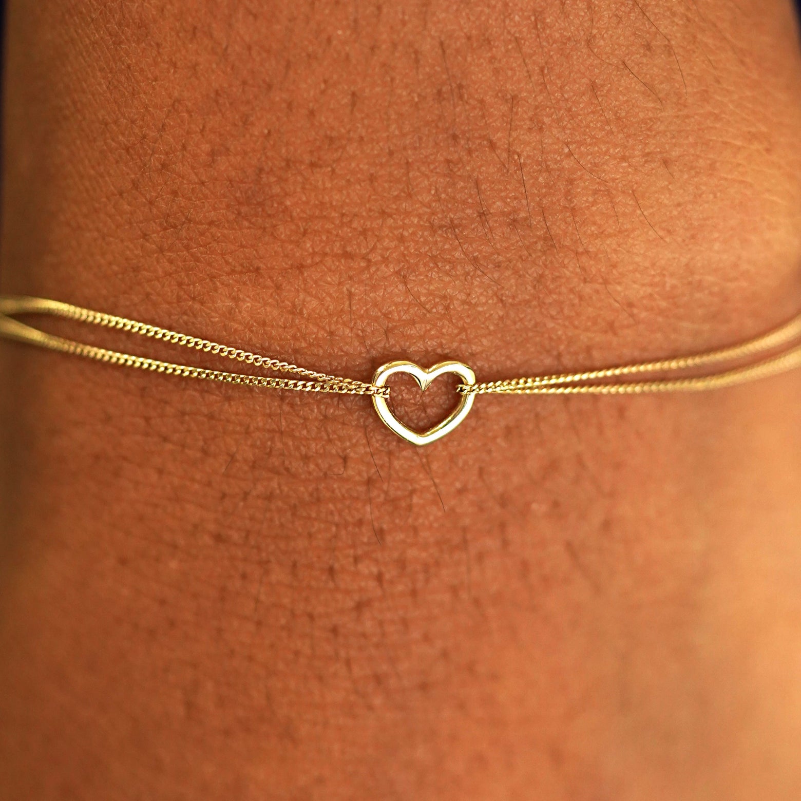 Close up view of a model's wrist wearing a solid yellow gold Heart Braceletv