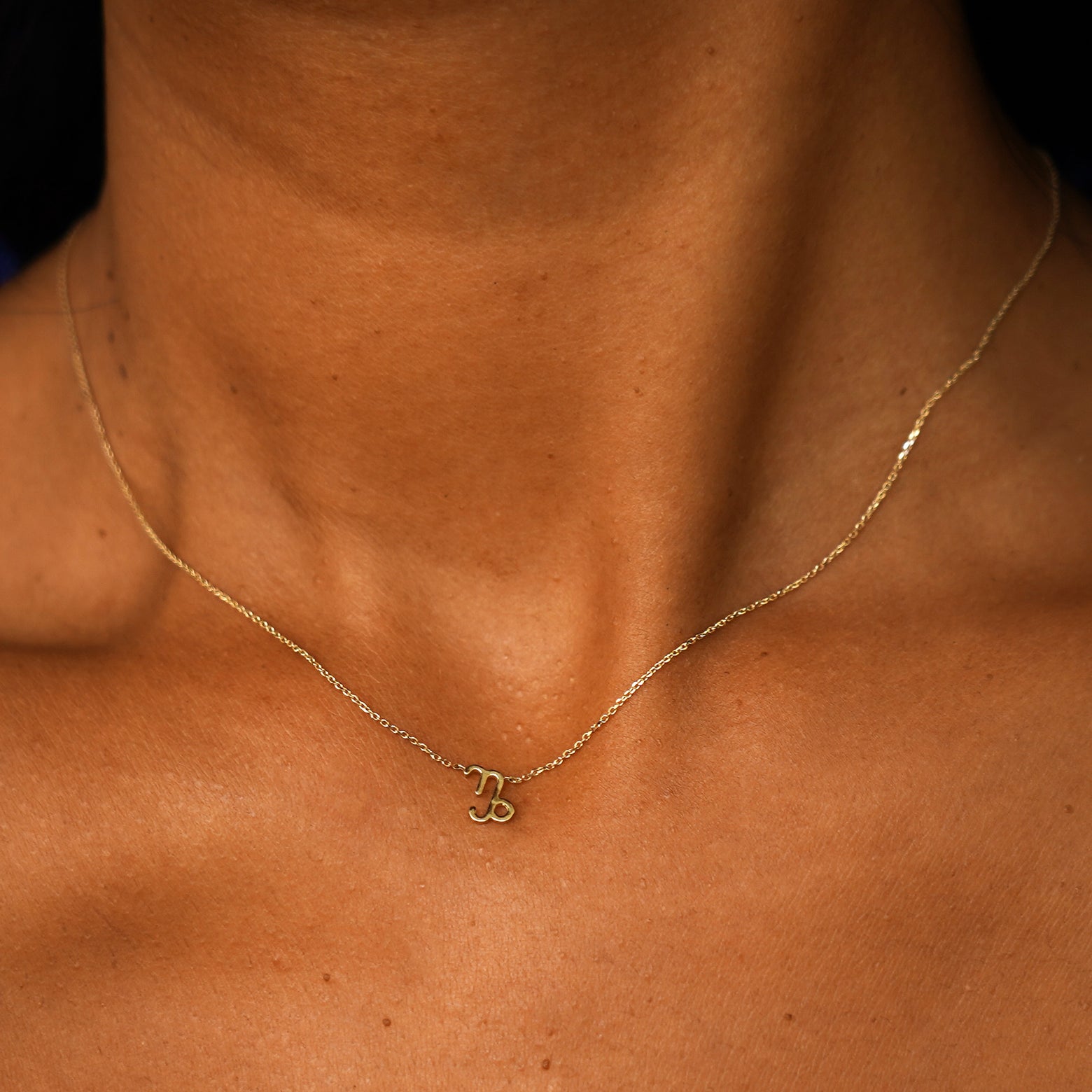 A model's neck wearing a solid 14k yellow gold Capricorn Horoscope Necklace
