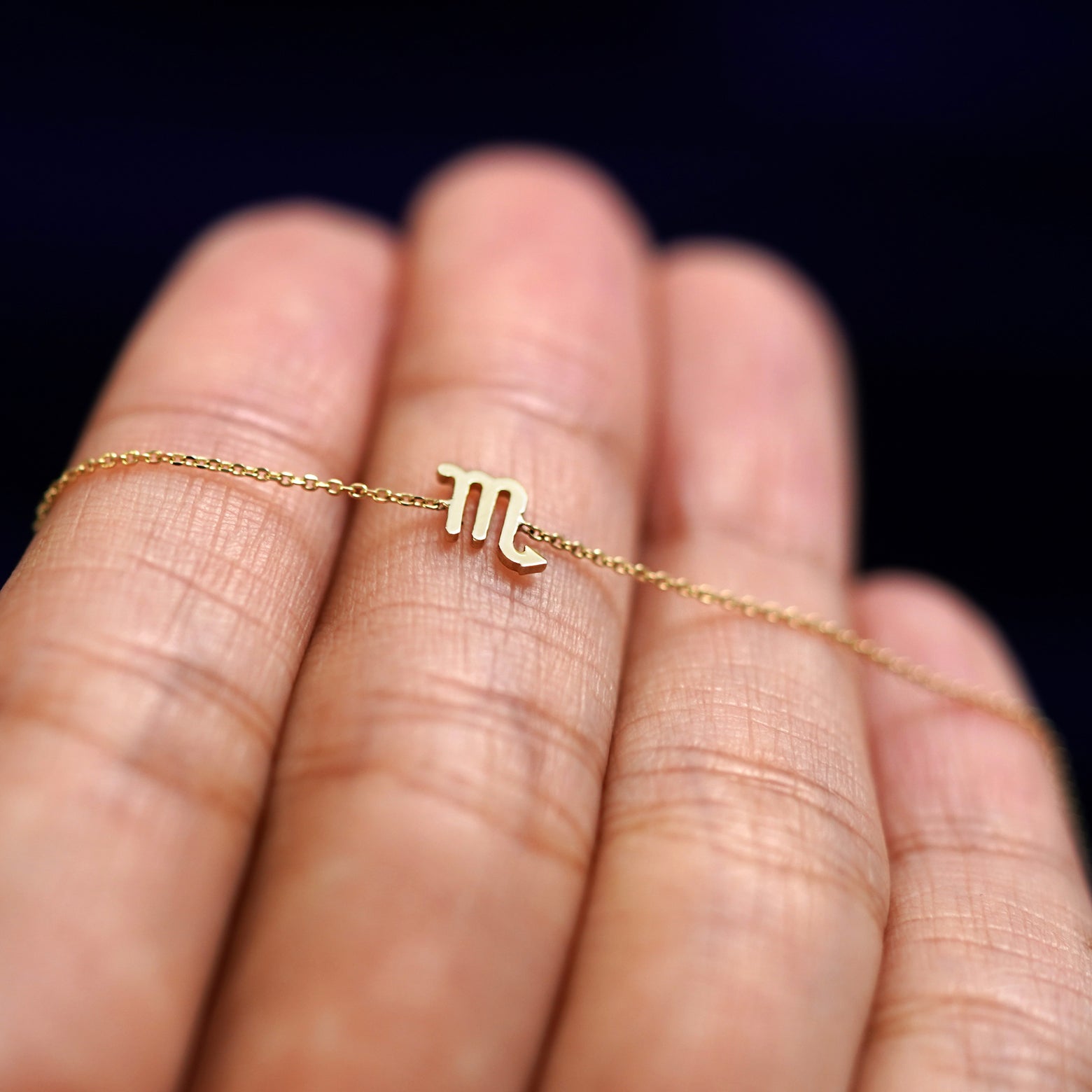 A yellow gold Scorpio Horoscope Bracelet resting on a model's fingers