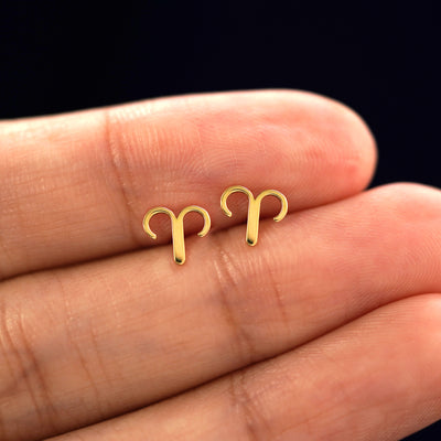 A model's hand holding a pair of recycled 14k gold Aries Horoscope Earrings