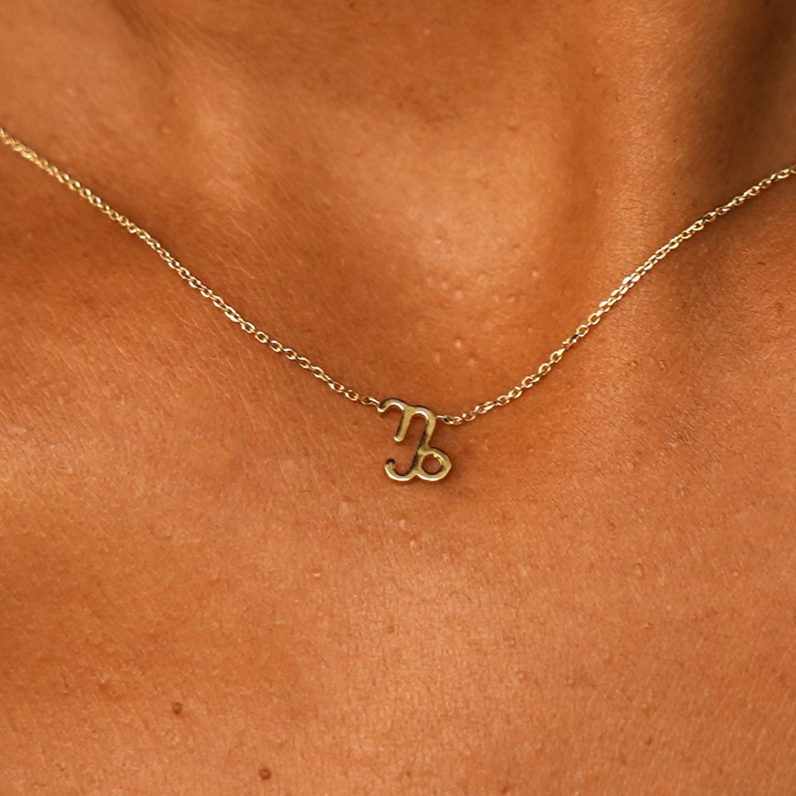 Close up view of a model's neck wearing a solid 14k yellow gold Capricorn Horoscope Necklace