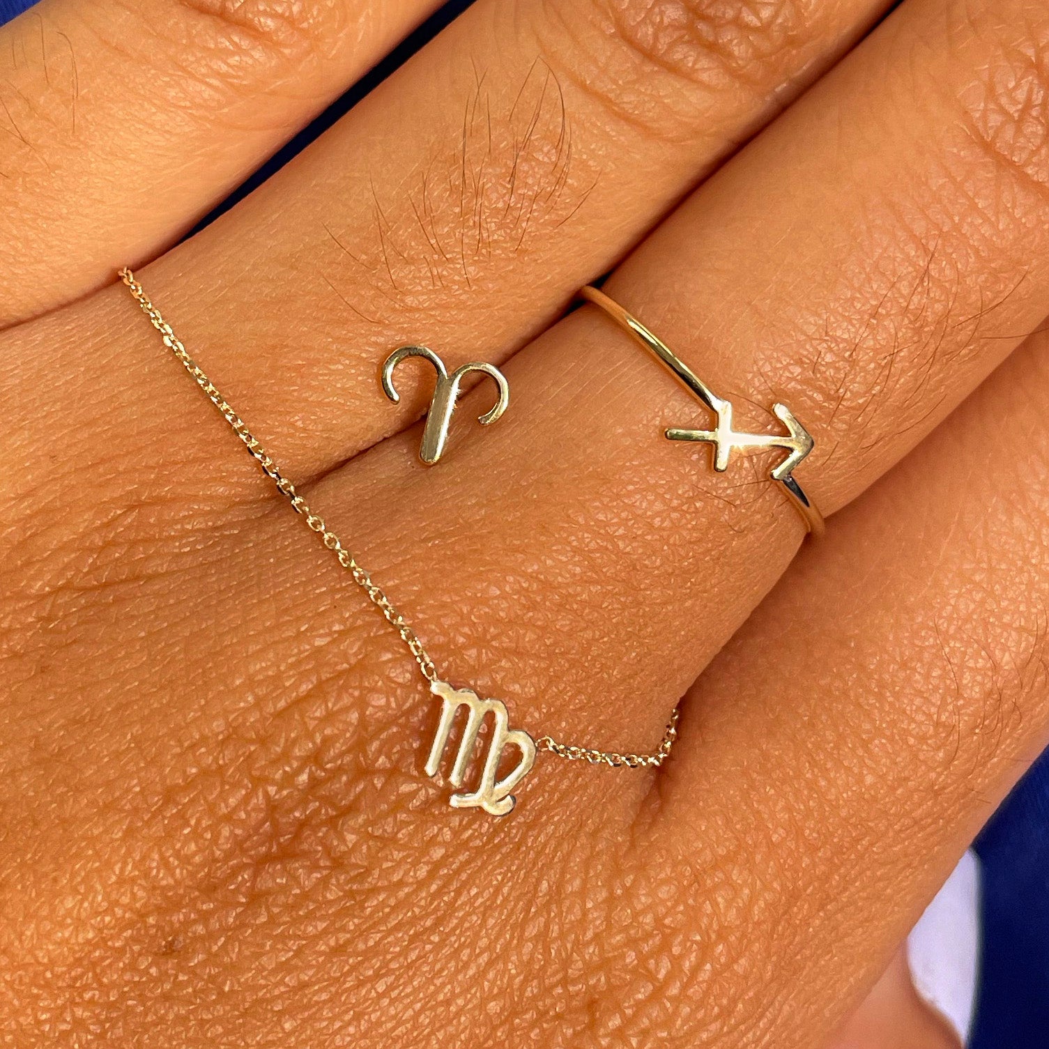 A hand holding a Horoscope bracelet, earring and ring in different zodiac signs