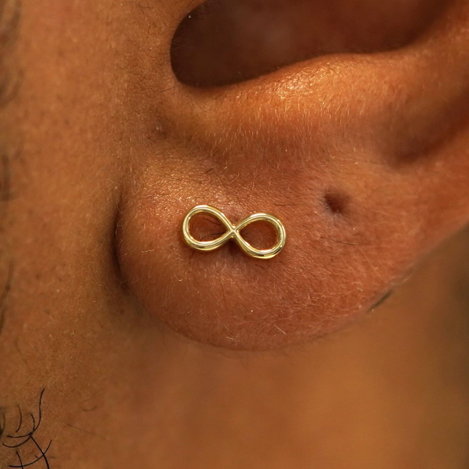 Close up view of a model's ear wearing a 14k gold Infinity Stud Earring