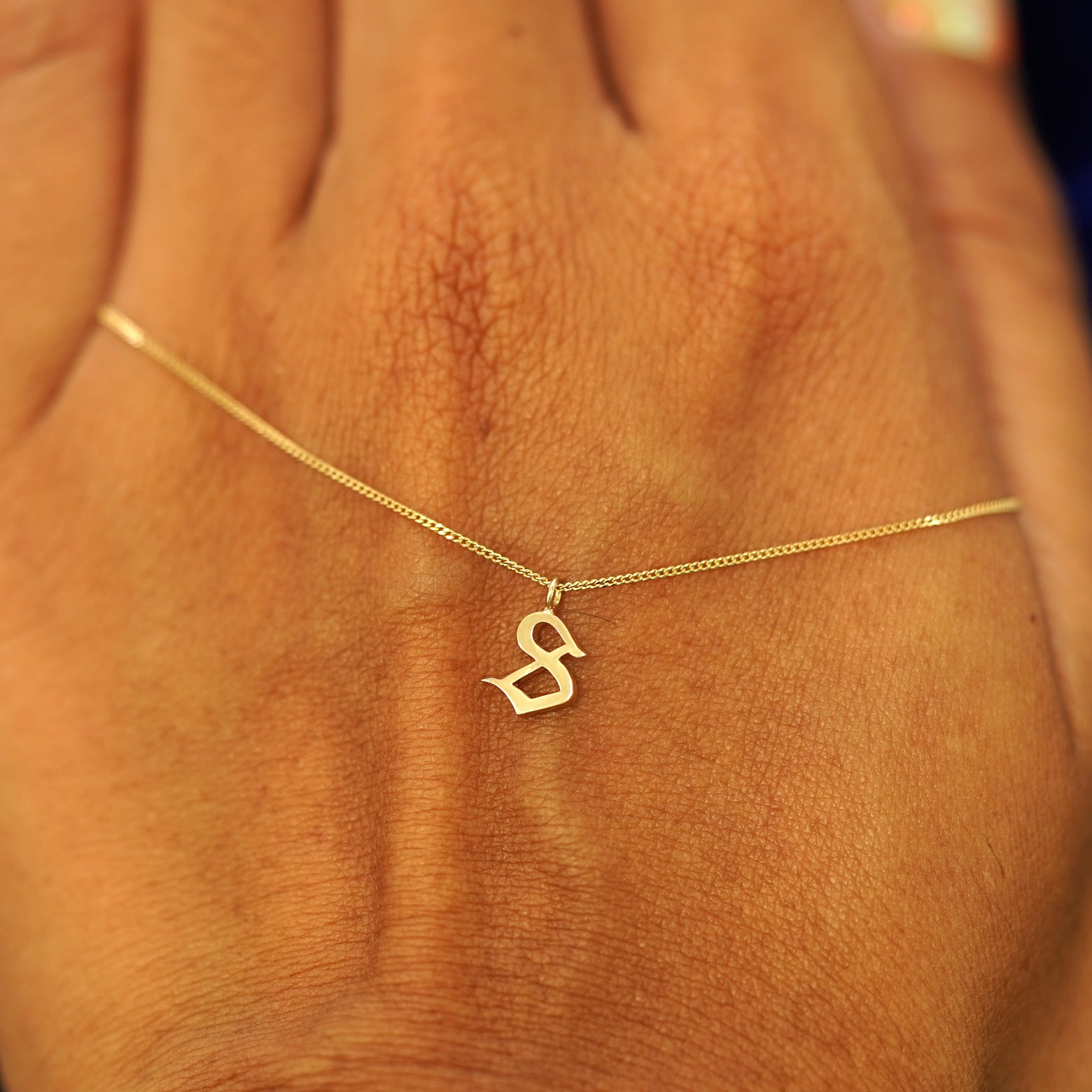 A solid 14k gold Initial Charm Necklace with the letter S draped across the back of a model's hand