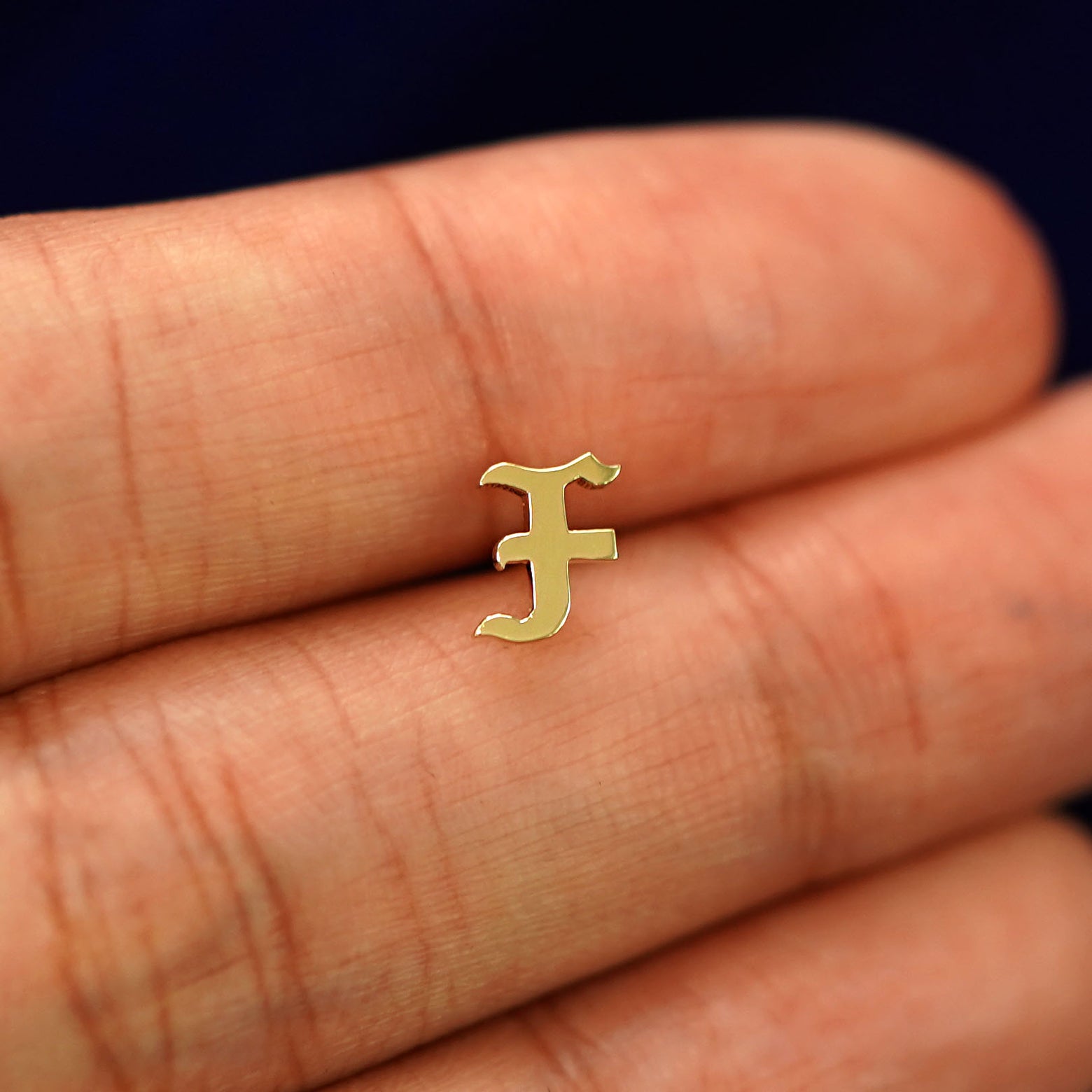 A solid yellow gold Initial Earring  in the letter F held in between model's fingertip to show the detail of the intial