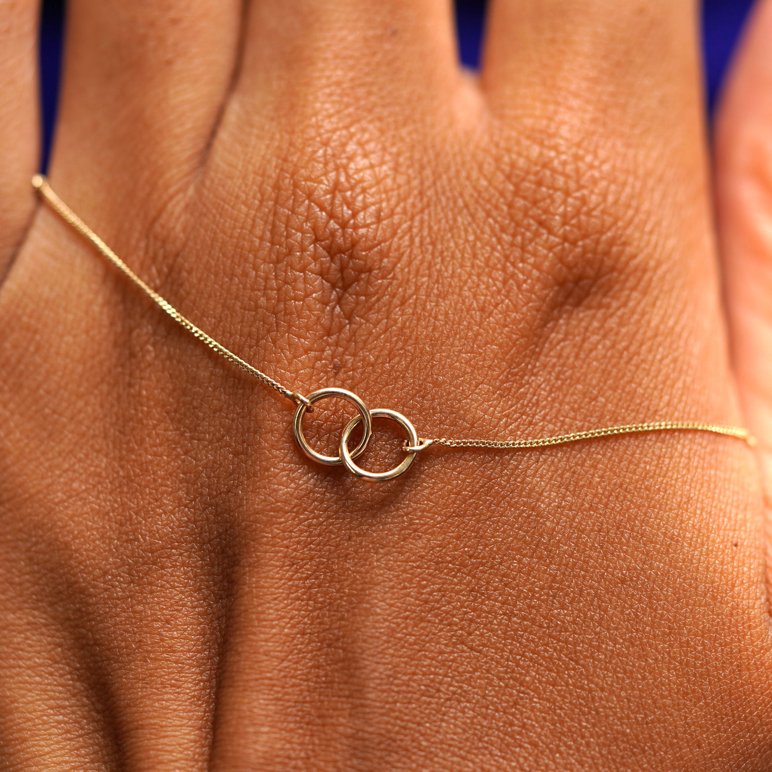 A solid gold Mini Bound Together Bracelet resting on the back of a model's hand