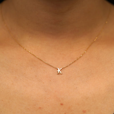 A model's neck wearing a 14k solid yellow gold Initial Necklace in the letter K
