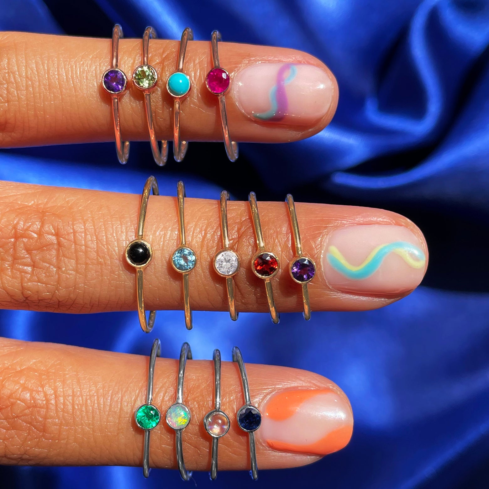 Three fingers with colorful wavy nail polish wearing various Automic Gold rings including a Moonstone Ring