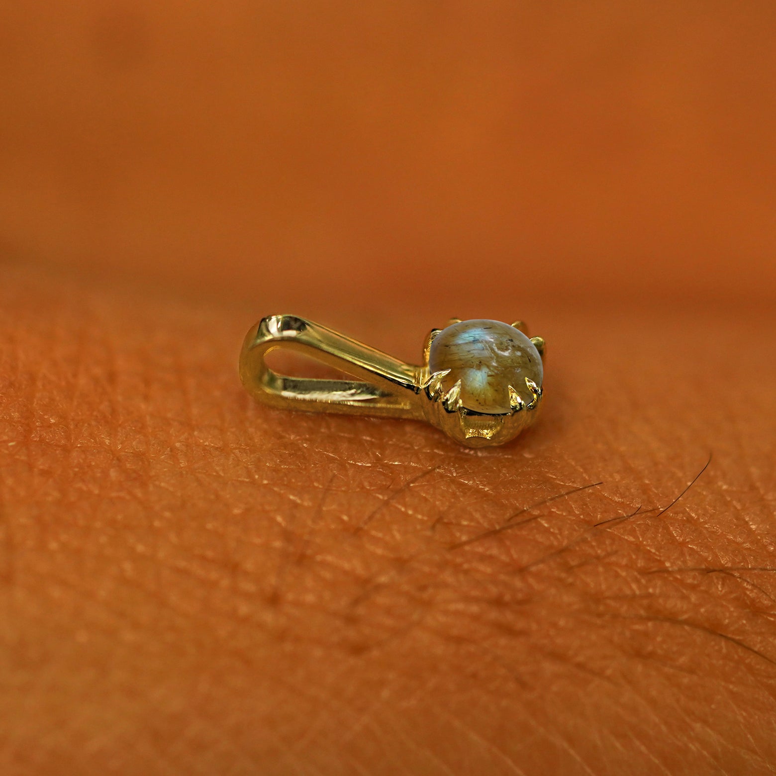 A 14k yellow gold Labradorite Charm for chain resting on the back of a model's hand