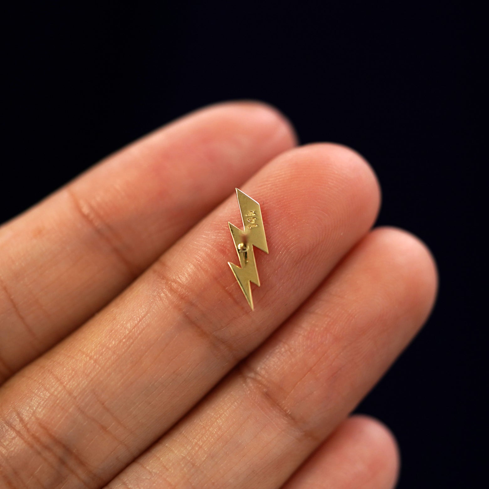 A yellow gold Lightning Bolt Earring laying facedown on a model's fingers to show the underside view