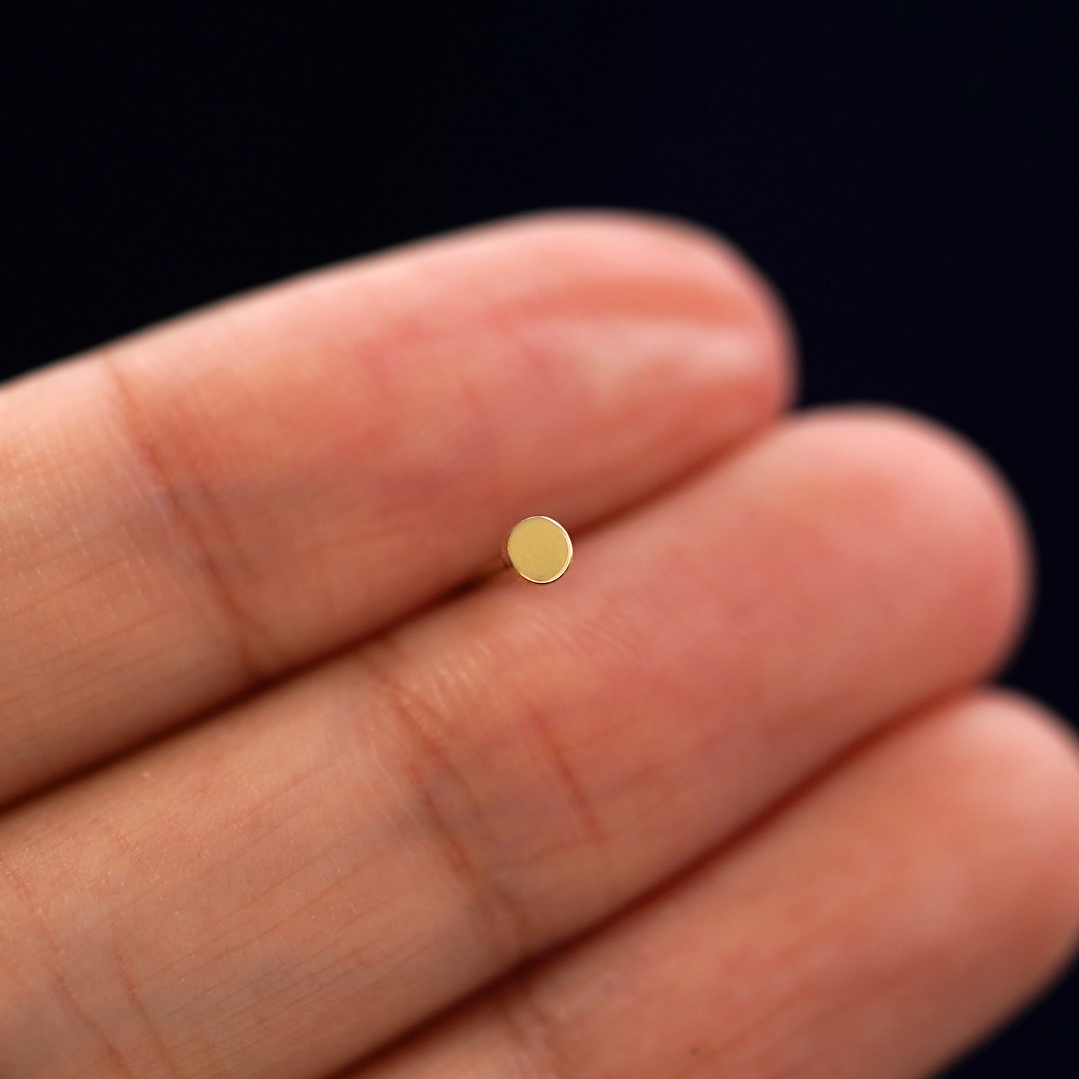 A solid 14k yellow gold Mini Circle Earring in between a model's fingers