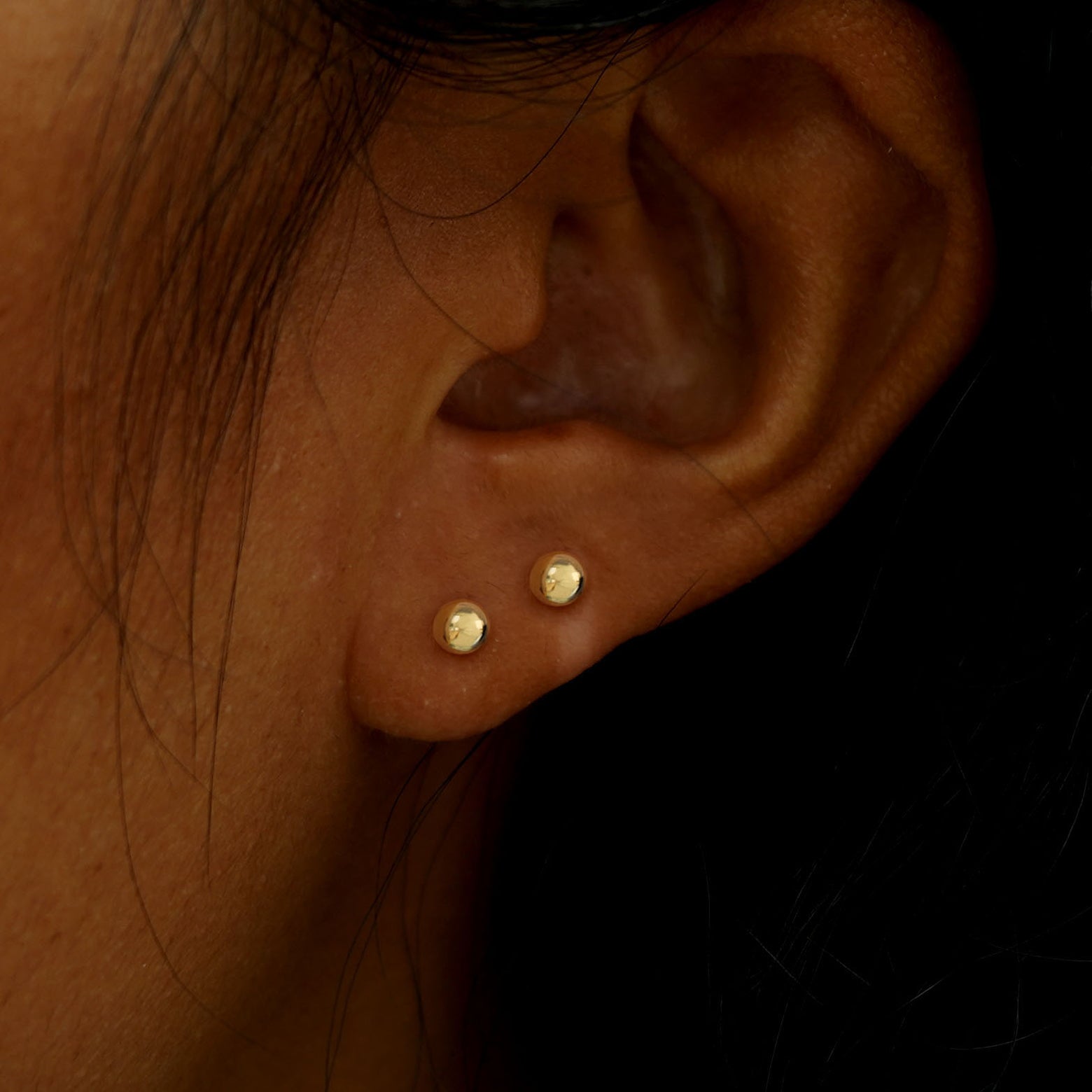 A model's ear wearing two 14k gold Medium Ball Earrings in two lobe piercings