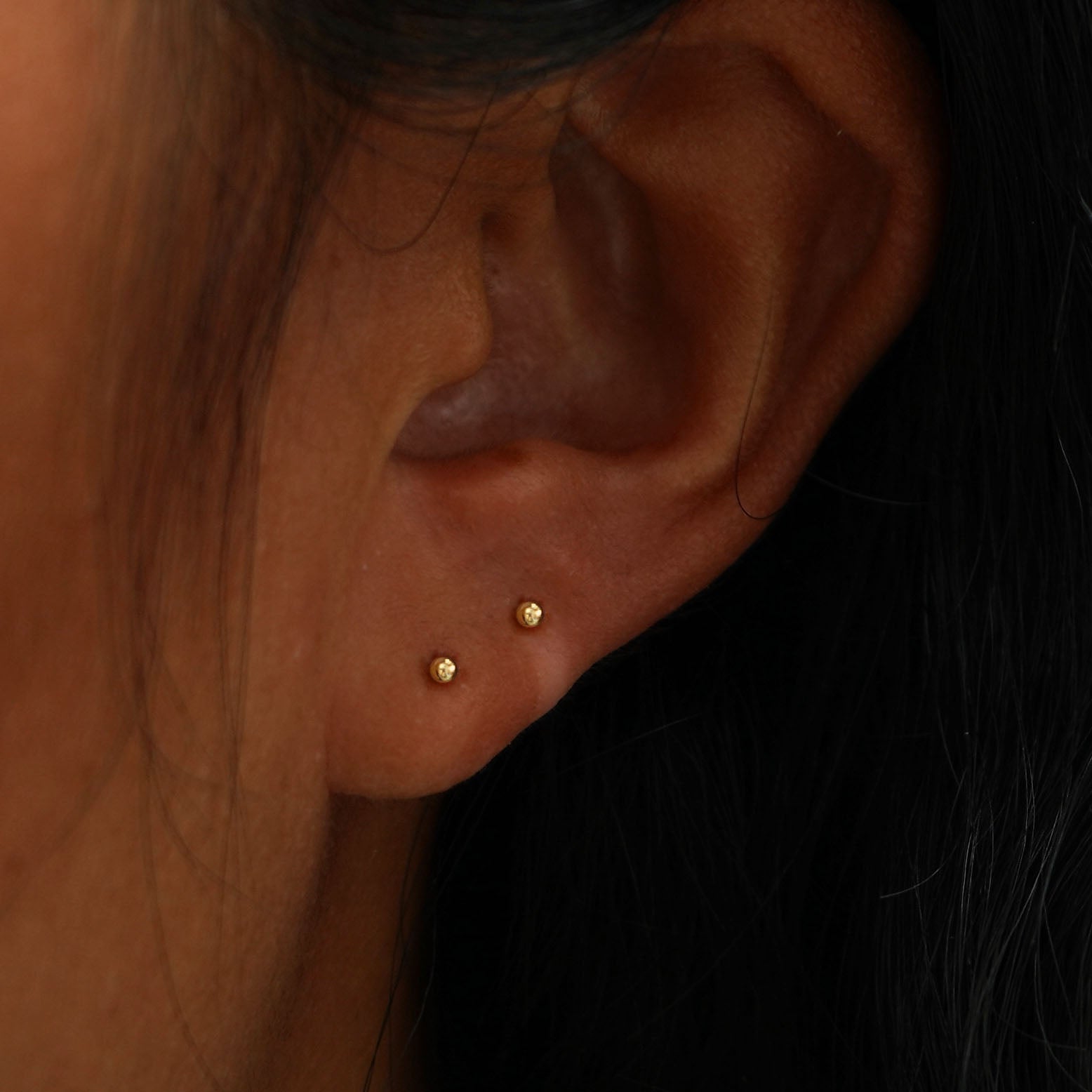 A model's ear wearing two 14k gold Mini Ball Earrings in two lobe piercings