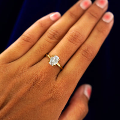 Close up view of a model's hand wearing a yellow gold Oval Moissanite Halo Ring