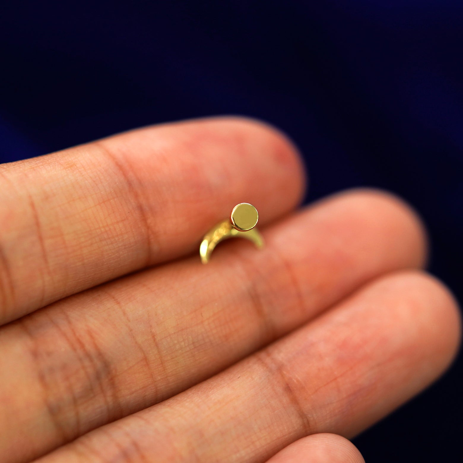 A solid yellow gold Moon Flatback Piercing laying facedown on a model's finger to show the end of the flat back