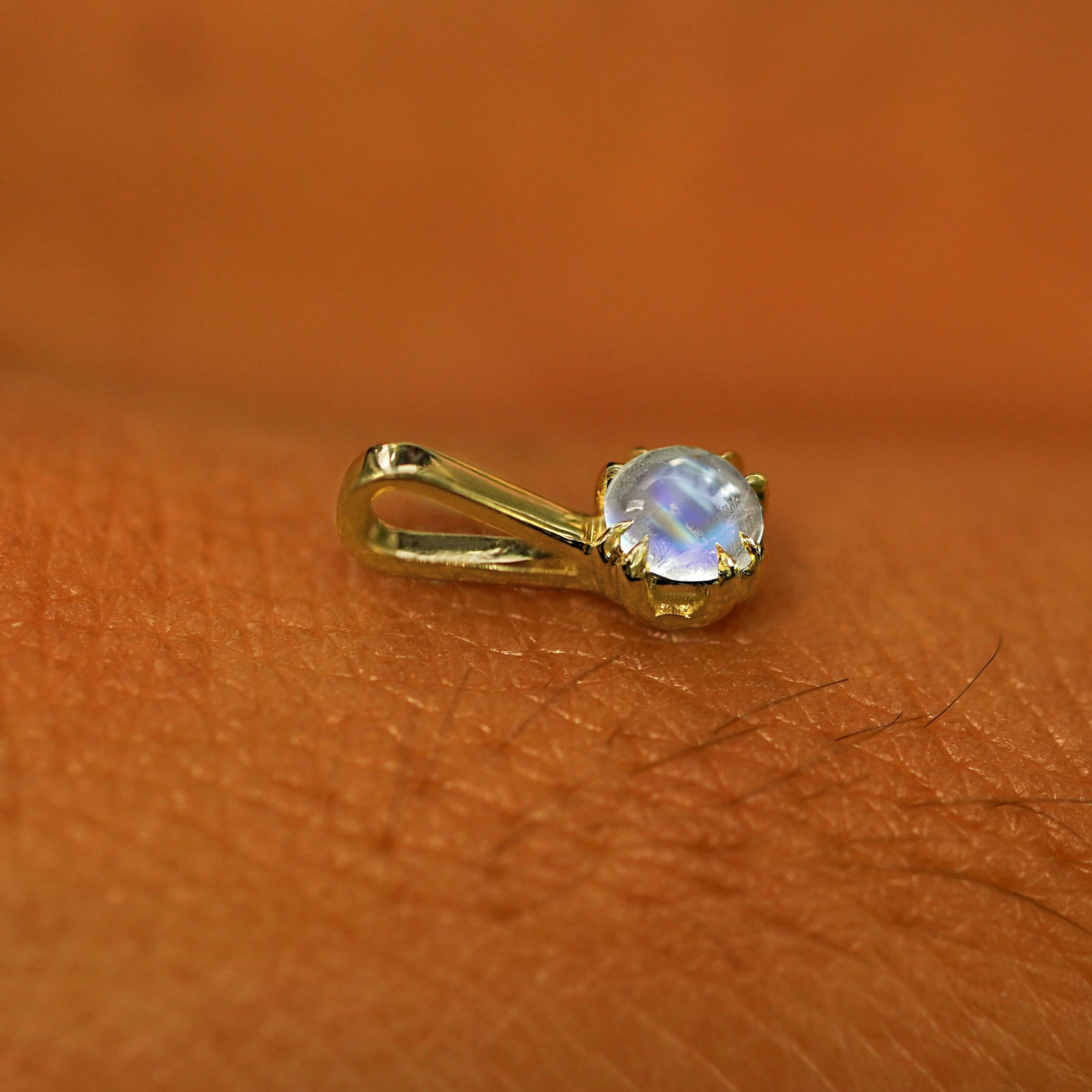 A 14k yellow gold Moonstone Charm for chain resting on the back of a model's hand