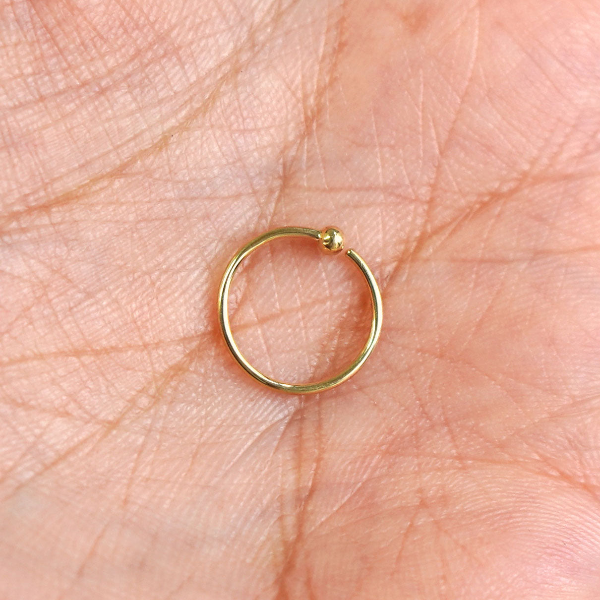 Close up view of a model's palm holding a single 14k solid gold Nose Ring Hoop