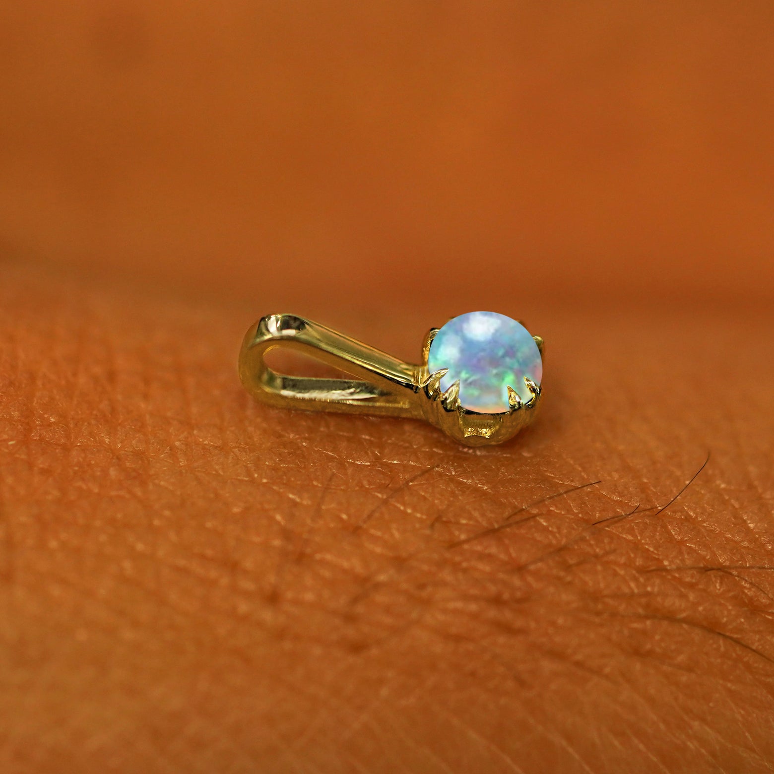A 14k yellow gold Opal Charm for chain resting on the back of a model's hand