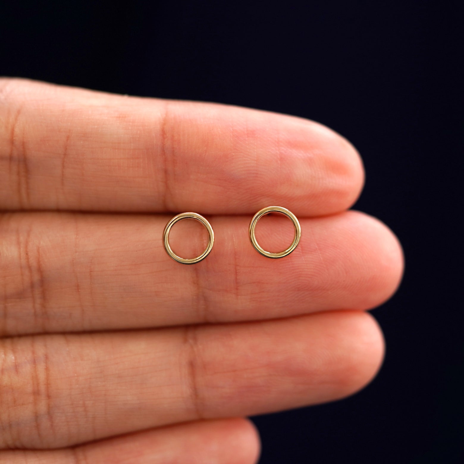 A model's hand holding a pair of recycled 14k gold Open Circle Earrings