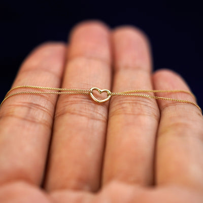A yellow gold Heart Bracelet resting on a model's fingers