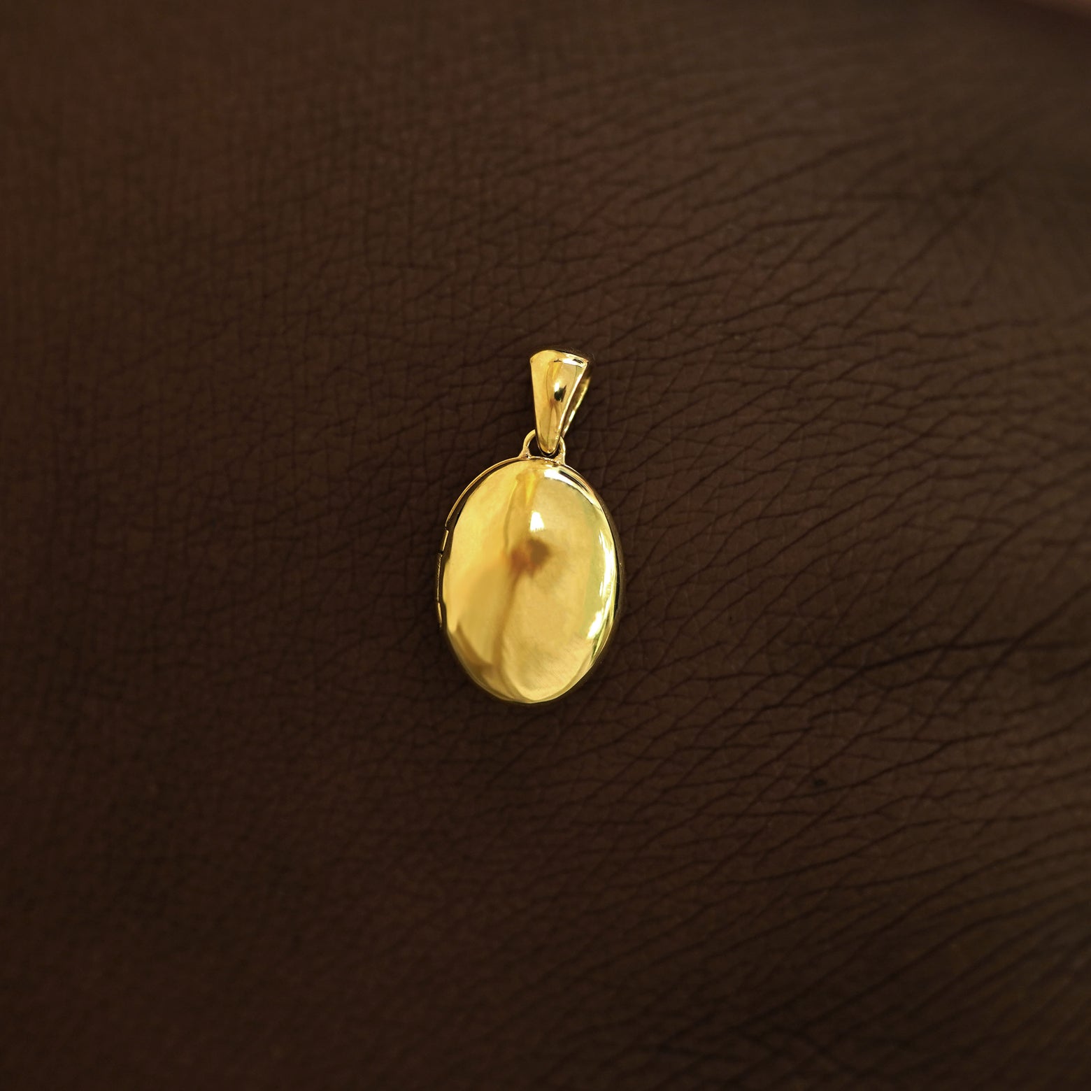 A closed 14k yellow gold Oval Locket Pendant on the back of a model's hand