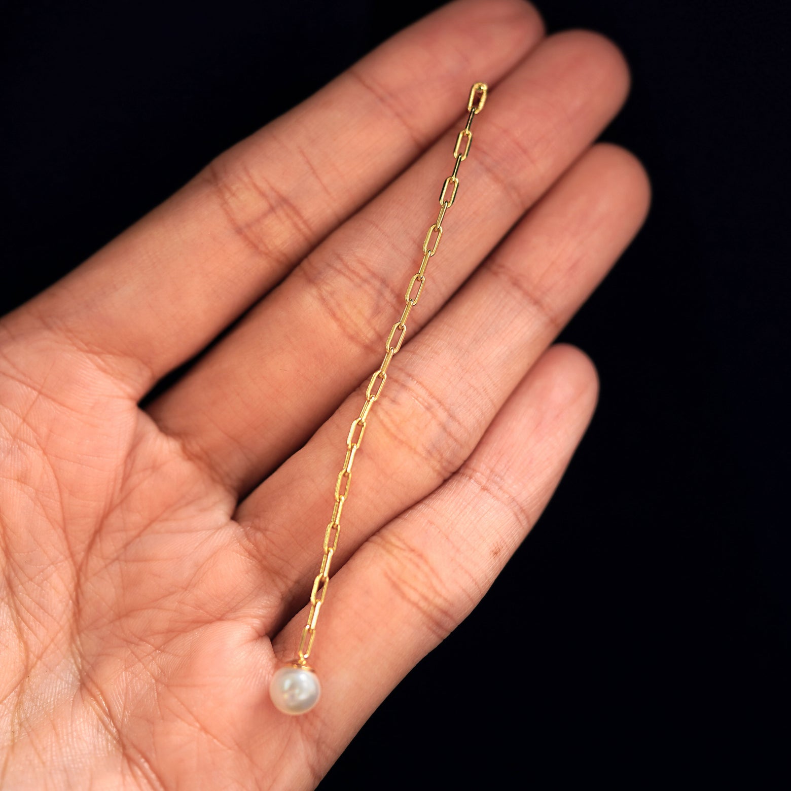 A 14k gold Pearl Dangle Earring held between a model's fingers to show the length of the butch chain
