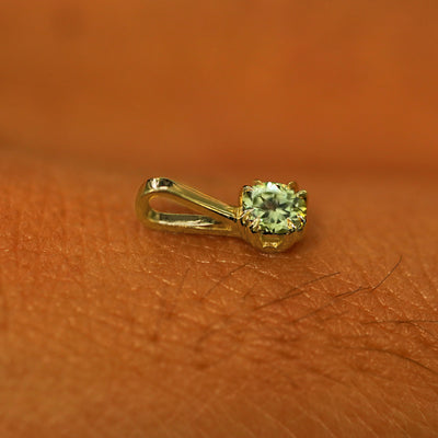 A 14k yellow gold Peridot Charm for chain resting on the back of a model's hand