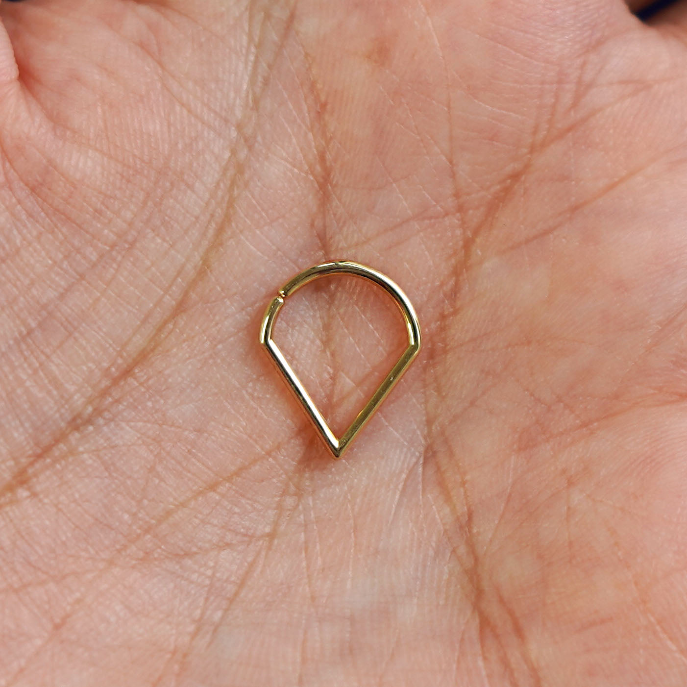 A model's hand holding a 14 karat yellow gold Pierced Triangle Septum