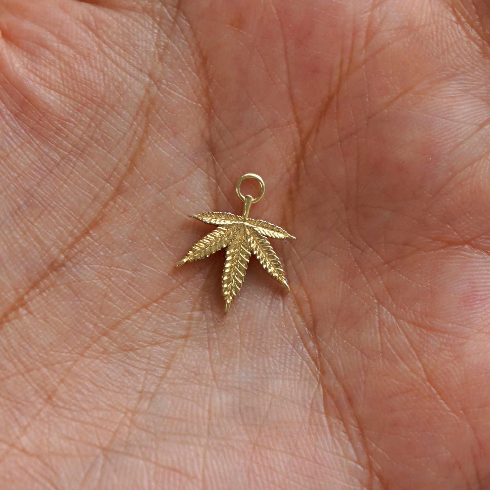 A solid gold Cannabis Charm for earring resting in a model's palm