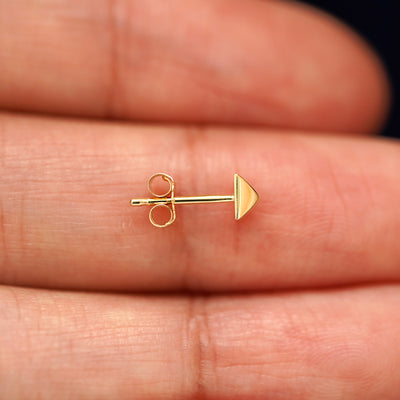 A 14k gold Pyramid Earring sitting sideways on a model's fingertips to show detail