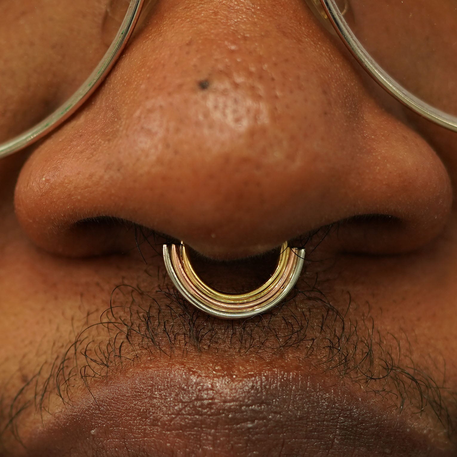 Close up view of a model's nose wearing a 14k solid gold Rainbow Septum