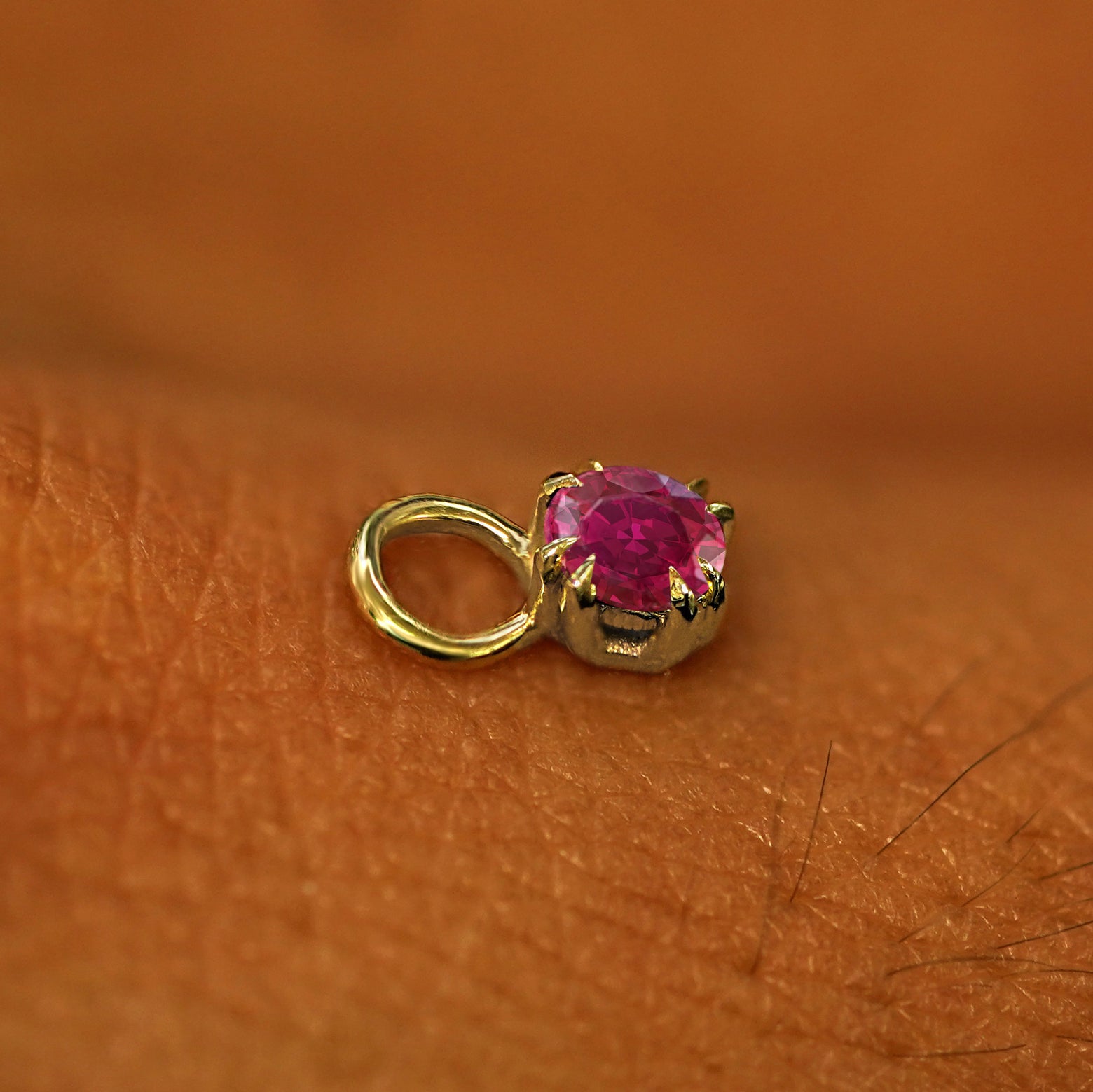 A solid yellow gold Ruby Charm for earring resting on the back of a model's hand