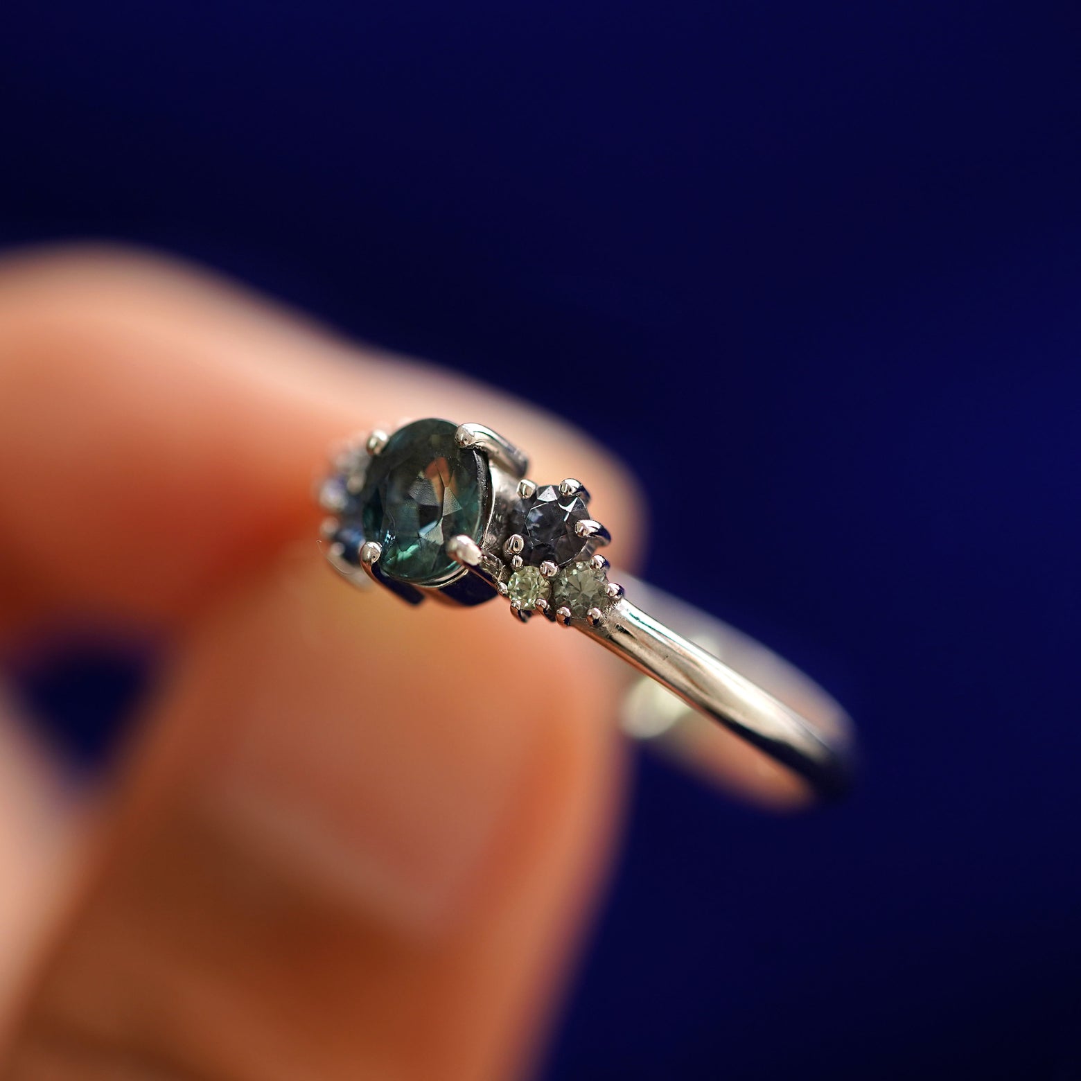 A model holding a Sapphire Cluster Ring tilted to show the side of the ring