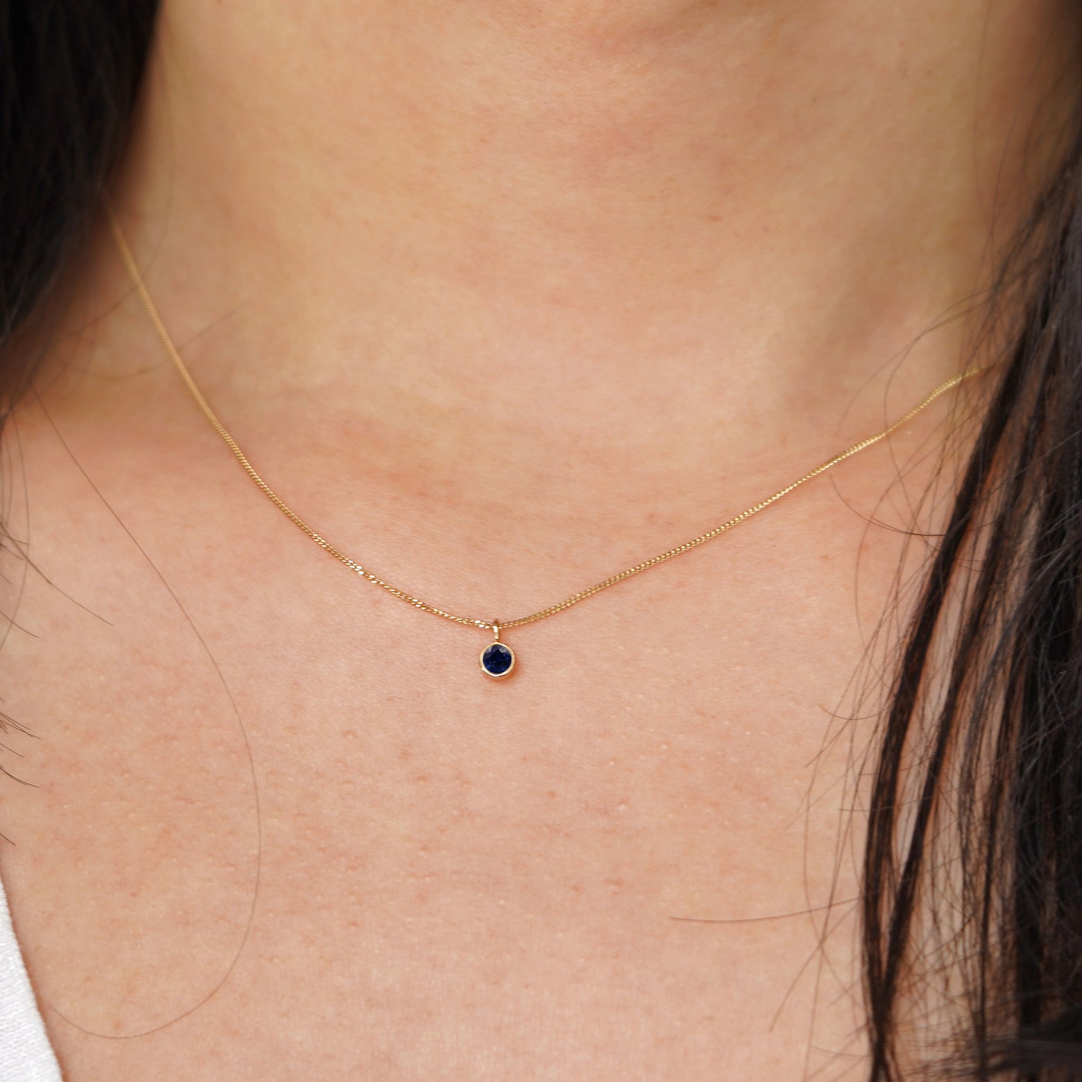 A model's neck wearing a solid 14k yellow gold Sapphire necklace