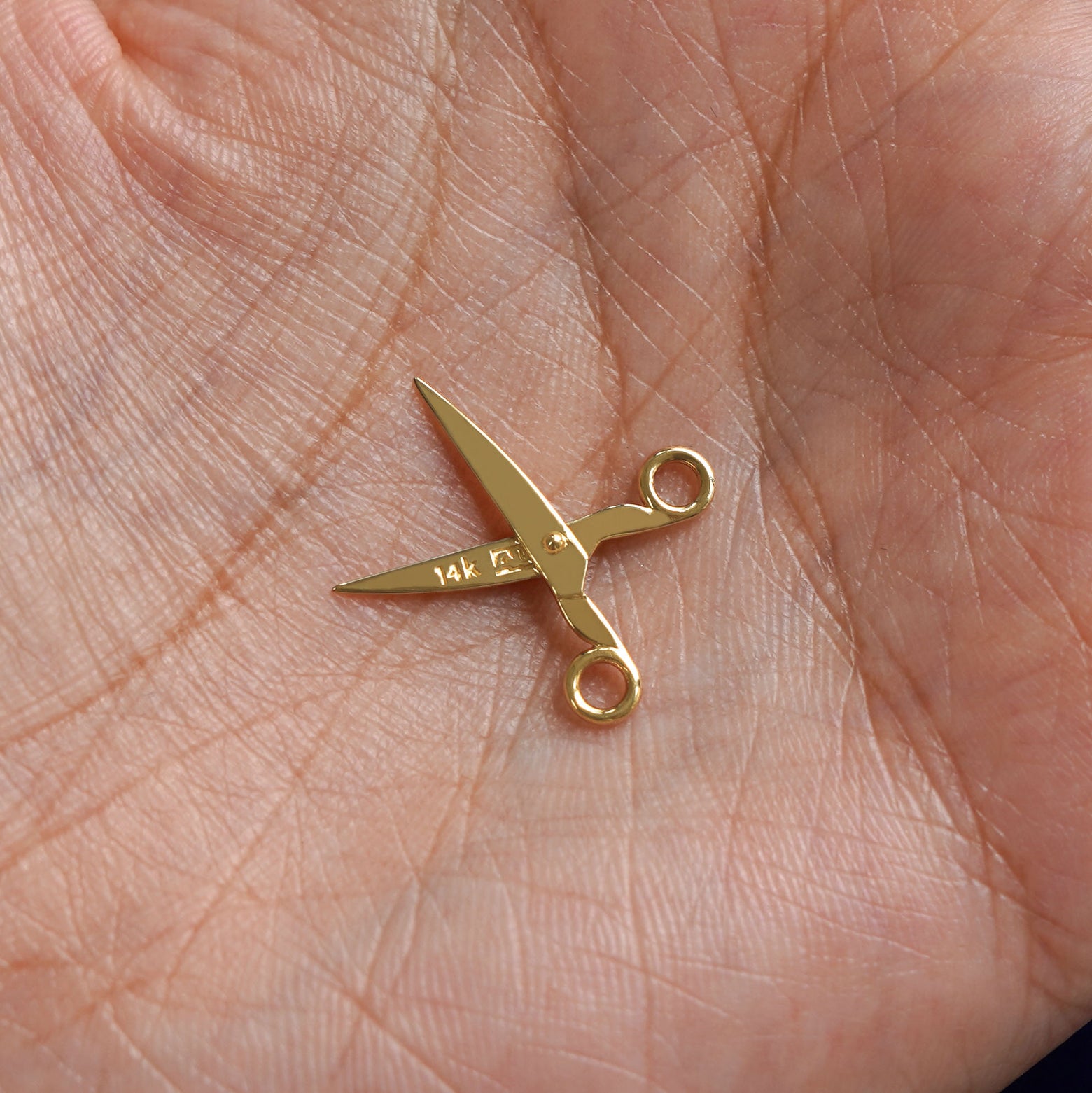 A 14k gold Scissors Charm for earring resting in a model's palm to show the back of the charm