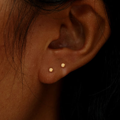 A model's ear wearing two 14k gold Small Ball Flatback Piercings in two lobe piercings