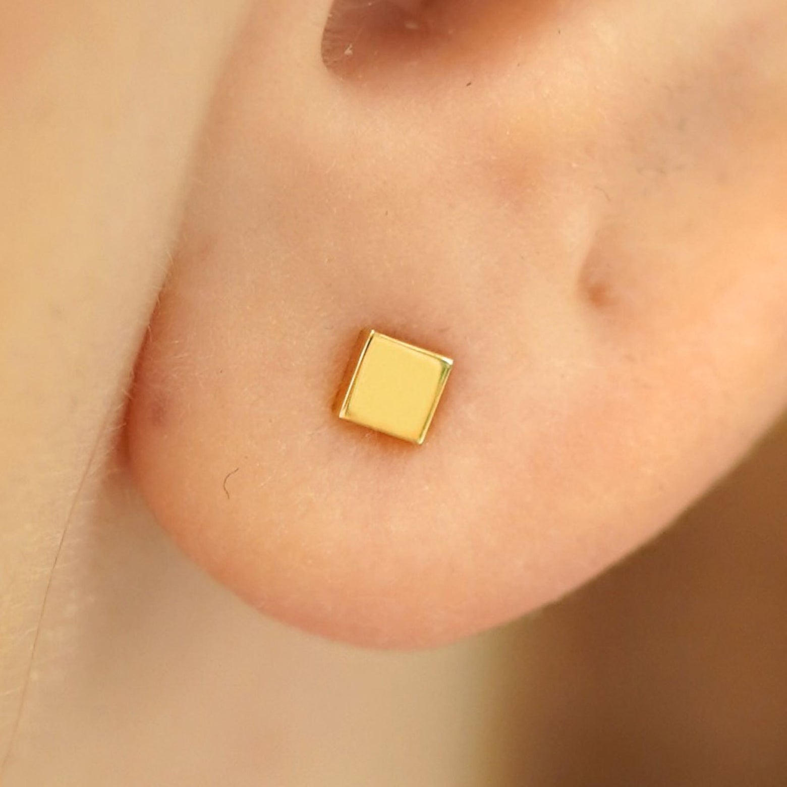 Close up view of a model's ear wearing a 14k gold Square Earring