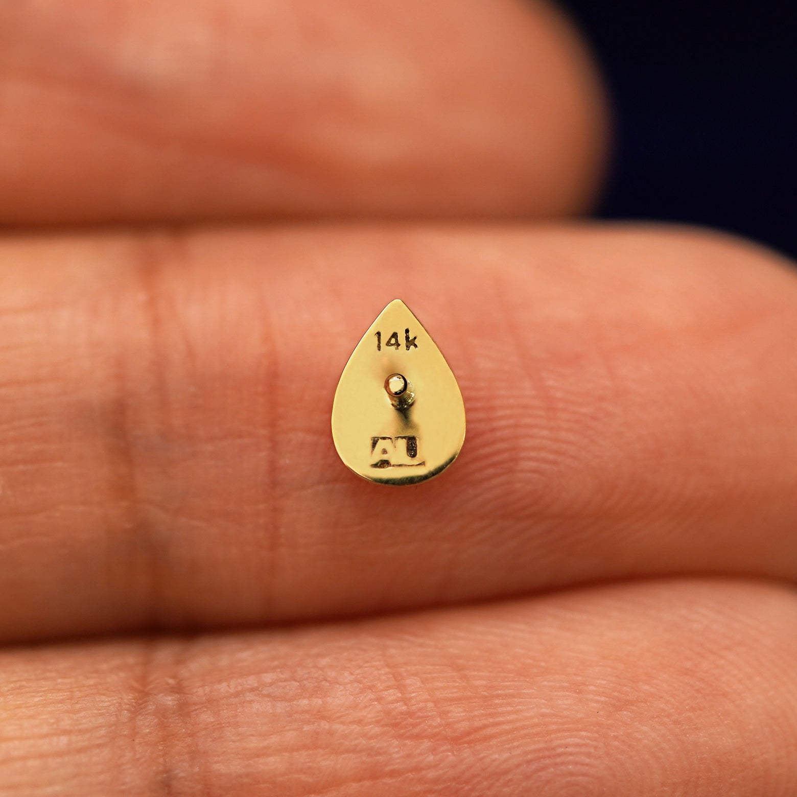 A yellow gold Teardrop stud laying facedown on a model's fingers to show the underside view