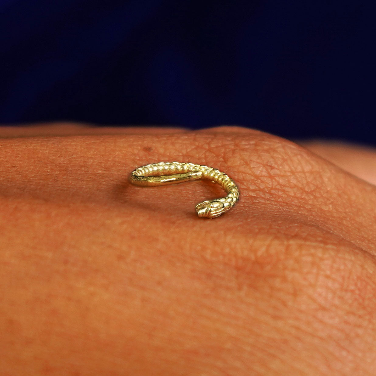 An open yellow gold Ouroboros Snake Hoops sitting on a model's knuckle