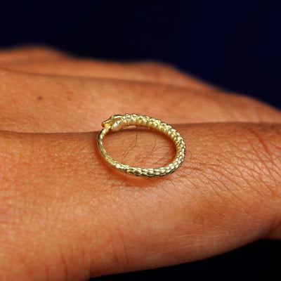 Side view of a 14k yellow gold Snake Hoop/ Piercing resting on the back of a model's finger