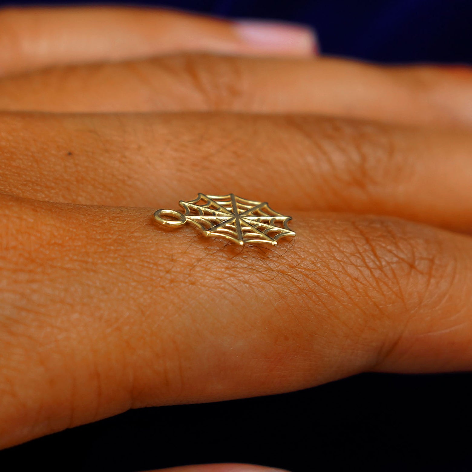 A 14k yellow gold Spider Web Charm for earring balancing on the back of a model's finger