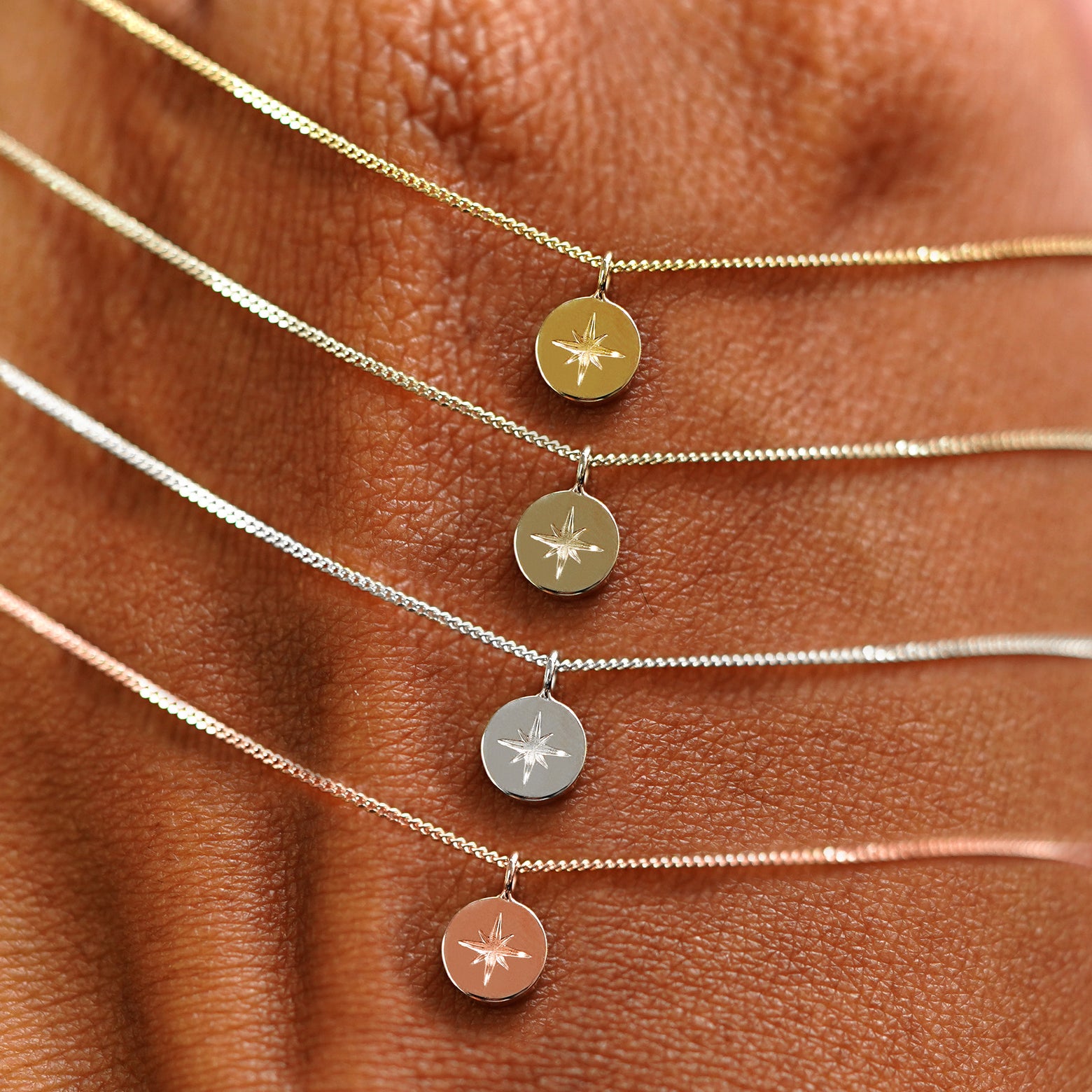 Four Star Disk Necklaces in options of yellow, champagne, white, and rose gold draped over the back of a model's hand