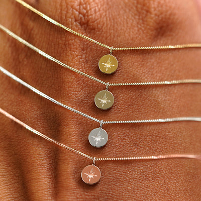 Four Star Disk Necklaces in options of yellow, champagne, white, and rose gold draped over the back of a model's hand