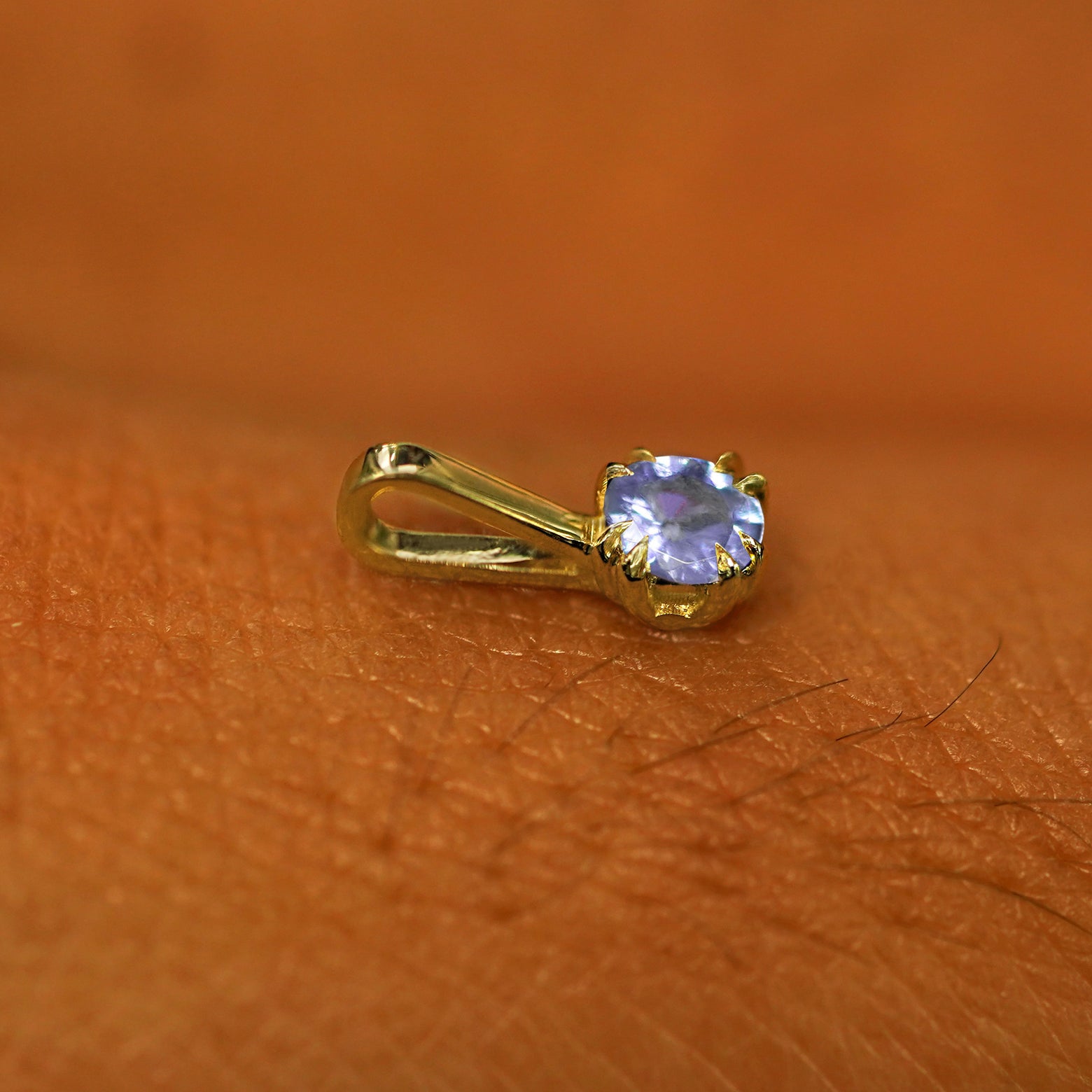 A 14k yellow gold Tanzanite Charm for chain resting on the back of a model's hand