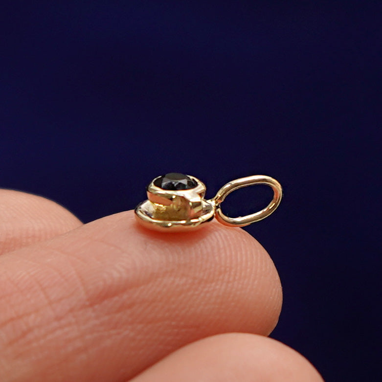 Side view of a 14k gold coffee cup charm on a model's fingertip