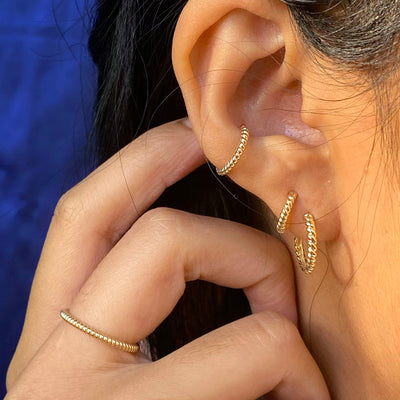 A model touching behind their ear wearing a yellow gold rope ring, rope cuff, and rope huggies