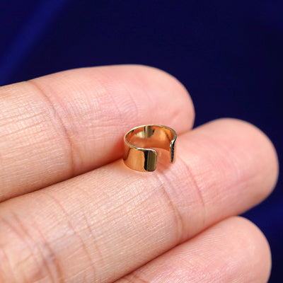 A solid yellow gold Thick Cuff earring resting on a model's fingertips