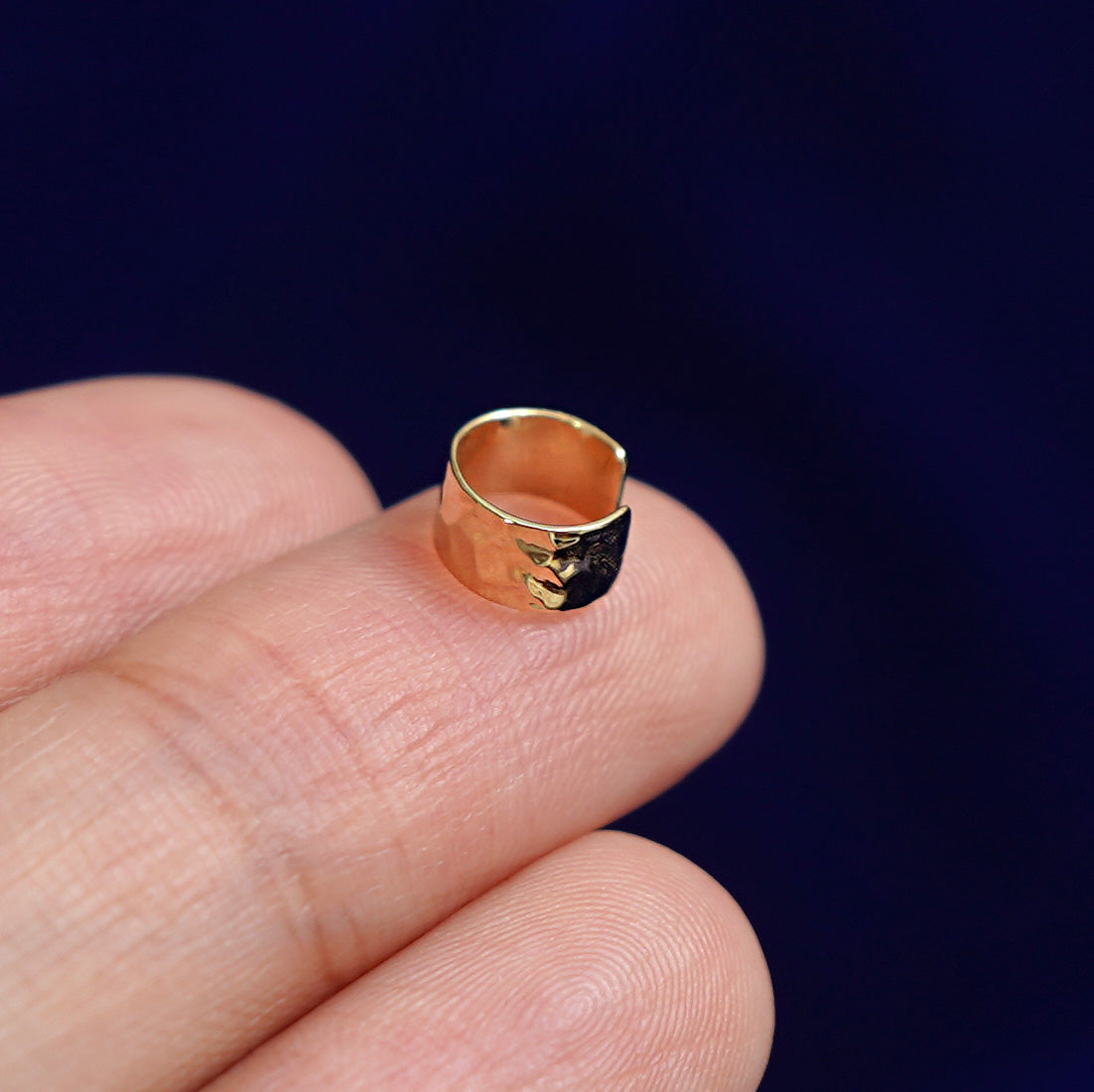 Alternate view of a solid yellow gold Thick Hammered Cuff earring resting on a model's fingertips