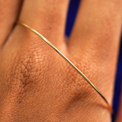 A solid gold Line Bangle Bracelet resting on the back of a model's hand